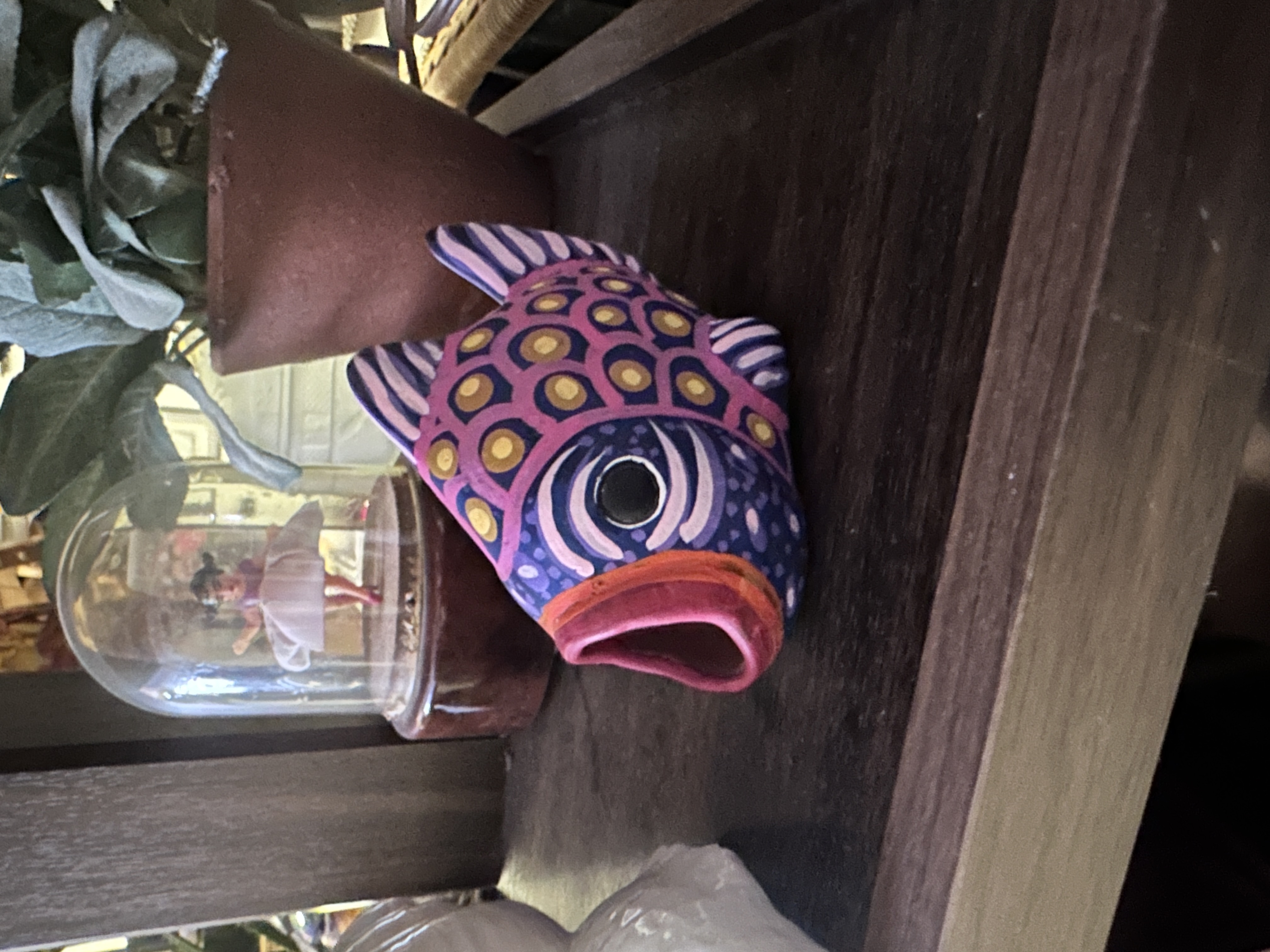 Colorful hand-painted fish-shaped wall pocket on a dark wood shelf